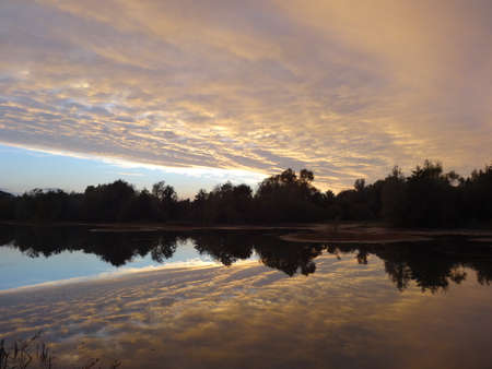 Sunset on the lake with clouds in the sky reflected in the waterの写真素材