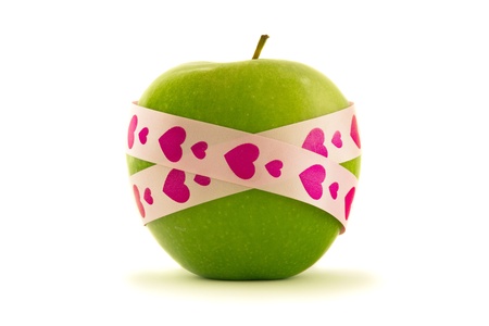 Green apple with pink heart pattern gift ribbon, isolated on whiteの写真素材