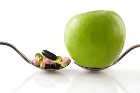 Serving spoon with green apple against a spoon full of pills, isolated on white backgroundの写真素材