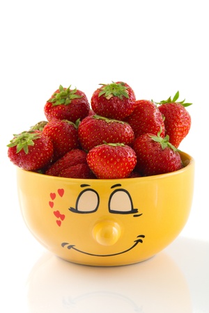 Large yellow cup with a shy face print full of ripe strawberries, isolated on a white background.の写真素材