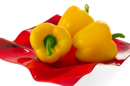 Three yellow bell pepper on a red plate, isolated on white background.の写真素材