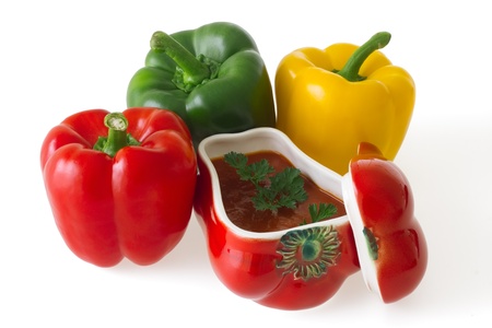 Red, green and yellow bell pepper with a ceramic ornament in shape of red pepper field with paprika ragout isolated on white backgroundの写真素材
