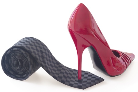 Red stiletto shoe standing on black rolled tie, concept of control, isolated on white backgroundの写真素材