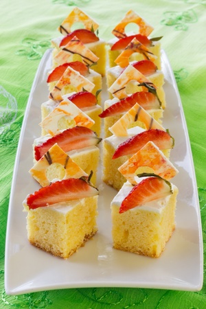 Group of Mini square sponge cakes with strawberries and white chocolate decoration on green background の写真素材