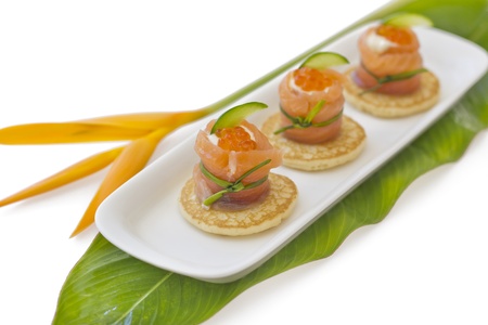 Red salmon roll with cheese, caviar and cucumber on blinis-base, isolated, on green leaf with tropical flower on the side  の写真素材