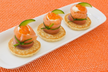 Red salmon roll with chees, caviar and cucumber on blinis base, on orange background の写真素材