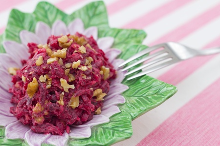 Beetroot and walnuts salad in flower shaped bowl on strapped pink background, with fork on the sideの写真素材
