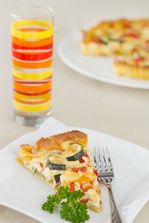 Slice of vegetable quiche garnish with parsley, and fork on the sideの写真素材