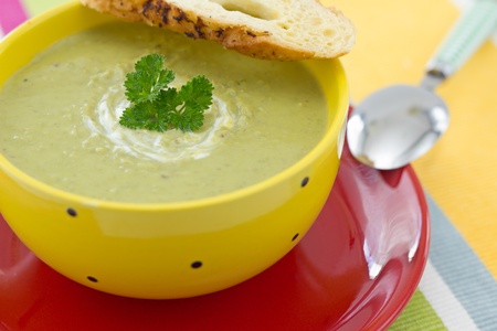 Green Pea cream soup with parsley and croutons, on red plateの写真素材