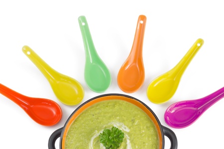 Green cream soup with parsley leaf sprig in a dark porcelain bowl with colorful spoons isolated over white background の写真素材