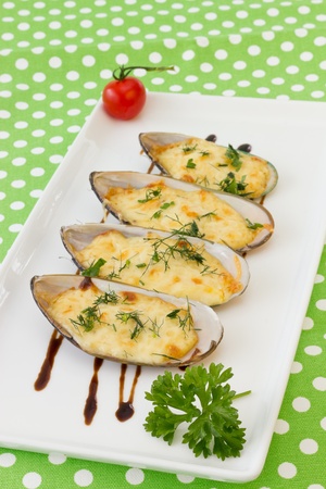 Baked Mussels under Cream Cheese Sauce  Garnished with dill and Cherry Tomato, on green polka dot backgroundの写真素材
