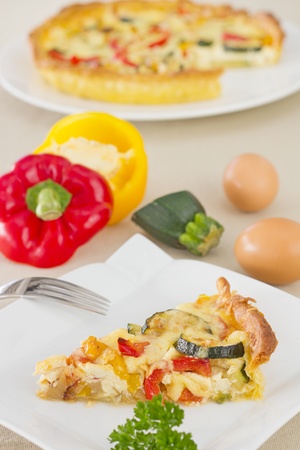 Slice of vegetarian quiche, decorated with parsley, with cut bell pepper and eggs on backgroundの写真素材