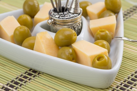 Green olives and cheese appetizer in a white triangular dishの写真素材