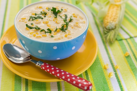 Cream of corn soup in blue bowl with fresh cob of corn on the sideの写真素材