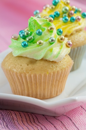 Two cupcakes  with yellow and green  buttercream and colorful decorations, on pink background の写真素材