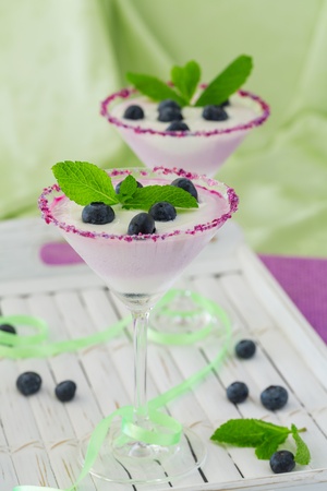 Fresh blueberry yogurt dessert in martini glasses and leafs of mint and blueberries for decorationの写真素材