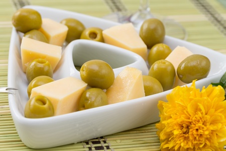 Green olives and cheese appetizer in a white triangular dishの写真素材
