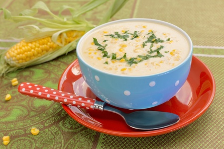 Cream of corn soup in blue bowl with fresh cob of corn on the sideの写真素材