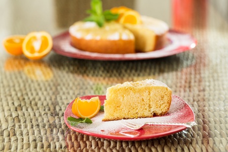 Slice of freshly cooked orange cake, with whole cake on backgroundの写真素材