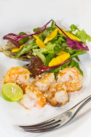 Fresh salad with fried shrimps, variety of salad leafs, mango, orange, lime, and toasted sesame の写真素材