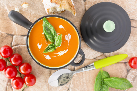 Top view of a Tomato soup in a black casserole, drizzled with cream and garnish with leaves of fresh green basil, on orange stone  backgroundの写真素材