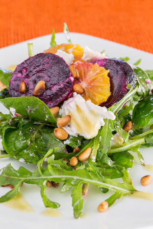 fresh salad with roasted beetroot, white cheese, orange and pine nuts, close-up, on orange backgroundの写真素材
