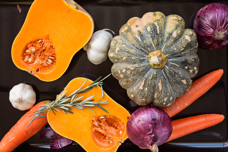 Pumpkin, carrot, onion, garlic and rosemary on black tray ready to roastの写真素材