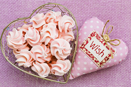 Pink meringue in heart shaped basket with soft fabric heart by,  on violet background, top viewの写真素材
