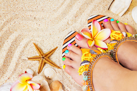 Female feet with pretty multicolor pedicure on sand, with frangipani flowers and seashells. Summertime conceptの写真素材