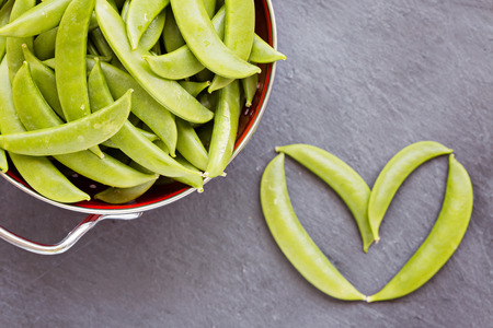 Green peas in red colander and single one on the sideの写真素材