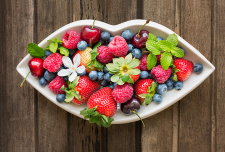 Mix of fresh berries on a white plate in shape of lips on wooden background top viewの写真素材