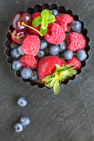 Mix of fresh berries in a small round metal backing mold, on stone gray background, top view, vertical compositionの写真素材