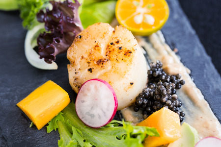 Pan seared scallops with salad, avocado, radish, mango and black caviar on a stone plate, close upの写真素材
