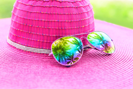 Pink summer hat and colorful sunglasses with palm tree reflectionの写真素材