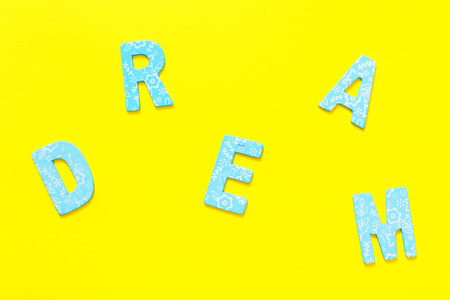 Word DREAM made out of small blue wooden letter on yellow background, flat layの写真素材