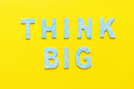 Word THINK BIG  made out of small blue wooden letter on yellow background, flat layの写真素材