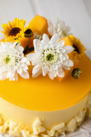 Mango cheesecake with yellow jelly topping, with flowers and fresh mango pieces on white backgroundの写真素材