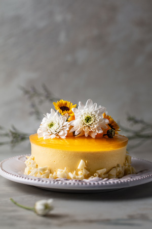 Mango cheesecake with yellow jelly topping, with flowers and fresh mango pieces on grey backgroundの写真素材