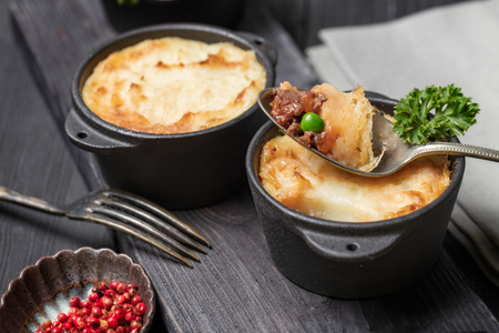 Shepherd's pie, british casserole in cast iron pan, with minced meat, mashed potatoes and vegetables, on dark backgroundの写真素材