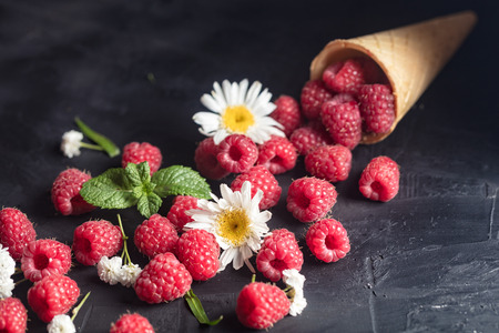 Fresh Deluxe Raspberries in ice cream cone with field flowers on dark wooden background.の写真素材