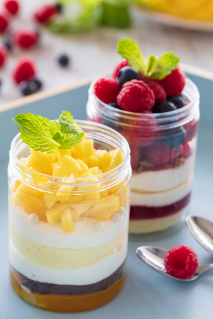 Raspberry and mango dessert, cheesecake, trifle, mouse in a glass jar on a light wooden background, vertical compositionの写真素材