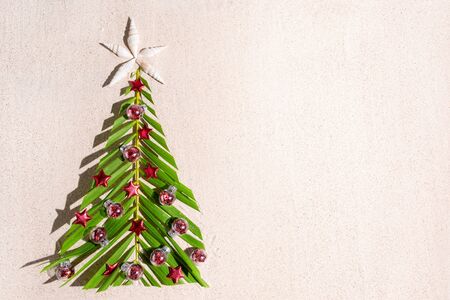Christmas tree made of green palm thee brunch with small red festive decorations on sand, top view, copy spaceの写真素材