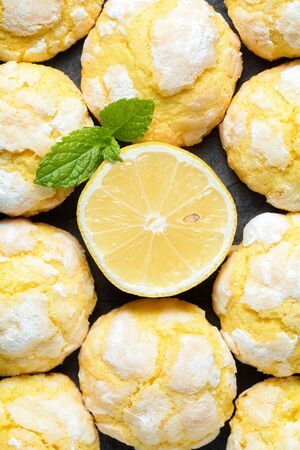 Background of freshly backed cracked crinkle Lemon cookies and slice of fresh lemon and mint leaf on dark background. Close up. Top view, vertical composition の写真素材