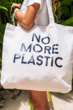 Young girl in white t-shirt  holding Eco bag NO MORE PLASTIC on tropical backgroundの写真素材