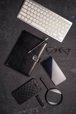Flat lay office desktop work space of wireless keyboard, pen, phone, magnifying glass and black reading glasses on black background, top view, copy space.の写真素材