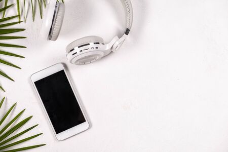 Flat lay office desktop work space of phone and white headphone with freen tropical leaves on white background , top view, copy spaceの写真素材