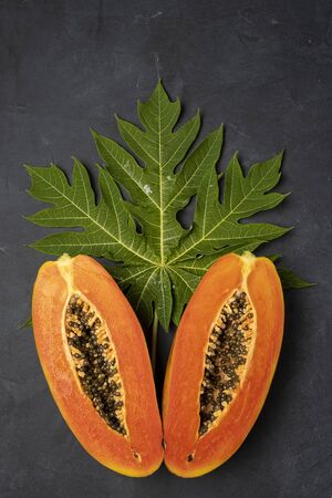 Two halfâs of freshly cut tropical papaya fruit, with green leaf on dark background, vertical composition の写真素材