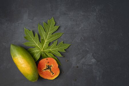 Ripe freshly cut papaya fruit with green papaya leaf  on black background, top view, copy spaceの写真素材