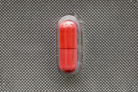 Single red medical  capsule in blister, macro, top view, medical conceptの写真素材