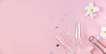 Two empty champagne glasses and bottle of champagne with white frangipani flowers and small heart decoration on pink background, copy spaceの写真素材